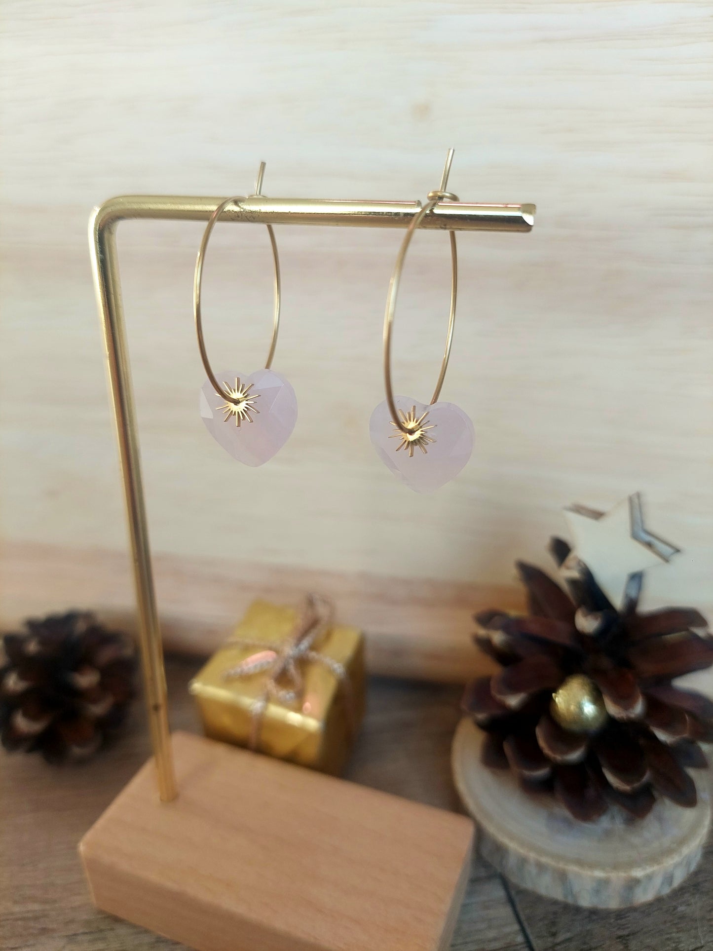 Créoles en quartz rose naturel avec pampille soleil dorée disposées sur un présentoir élégant.
