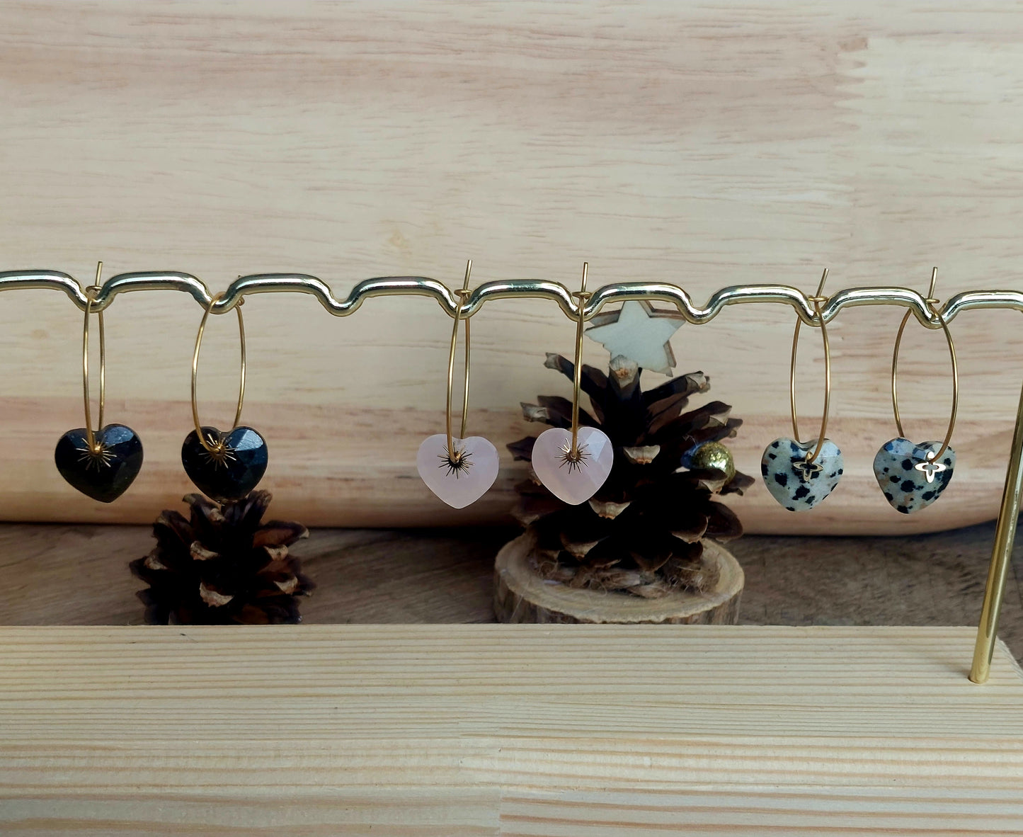 Créoles en acier inoxydable avec pendentifs en quartz rose, tourmaline noire et jaspe dalmatien, alignées sur un présentoir élégant.
