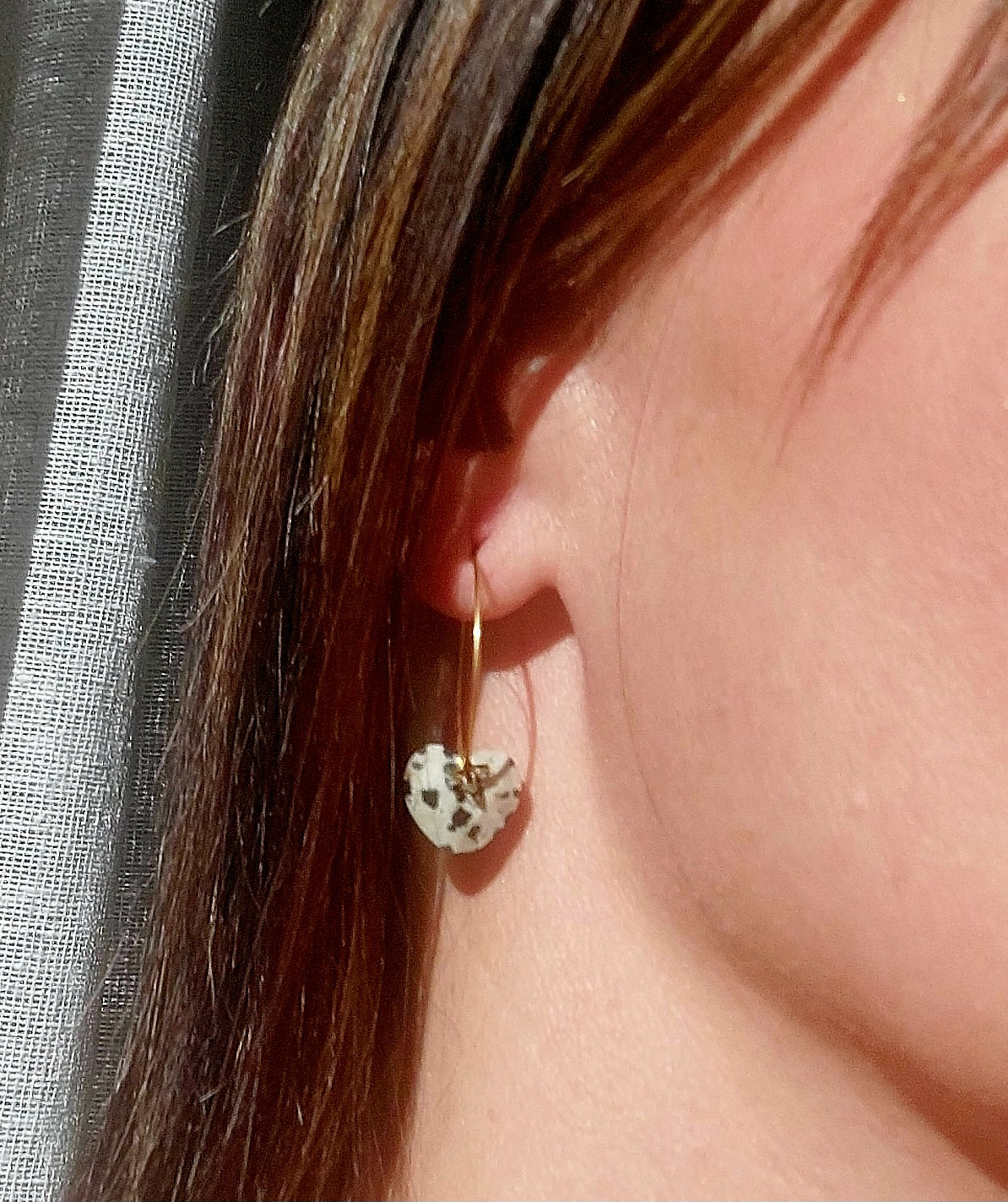 Créoles en acier inoxydable avec pierres jaspe dalmatien et pampille trèfle portées à l’oreille.