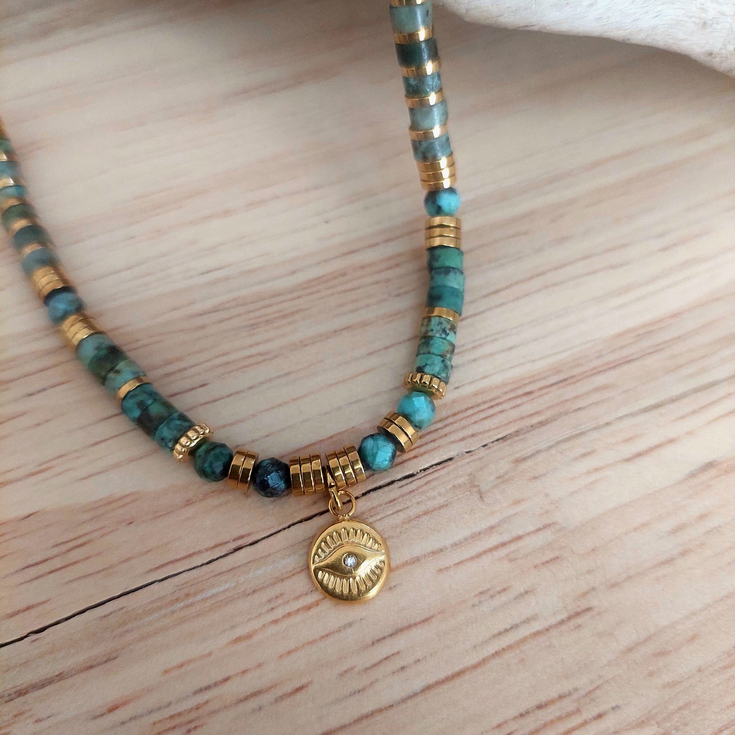 Collier en perles heishi turquoises africaines avec pendentif œil protecteur en gros plan – bijou fait main, modèle unique bohème.