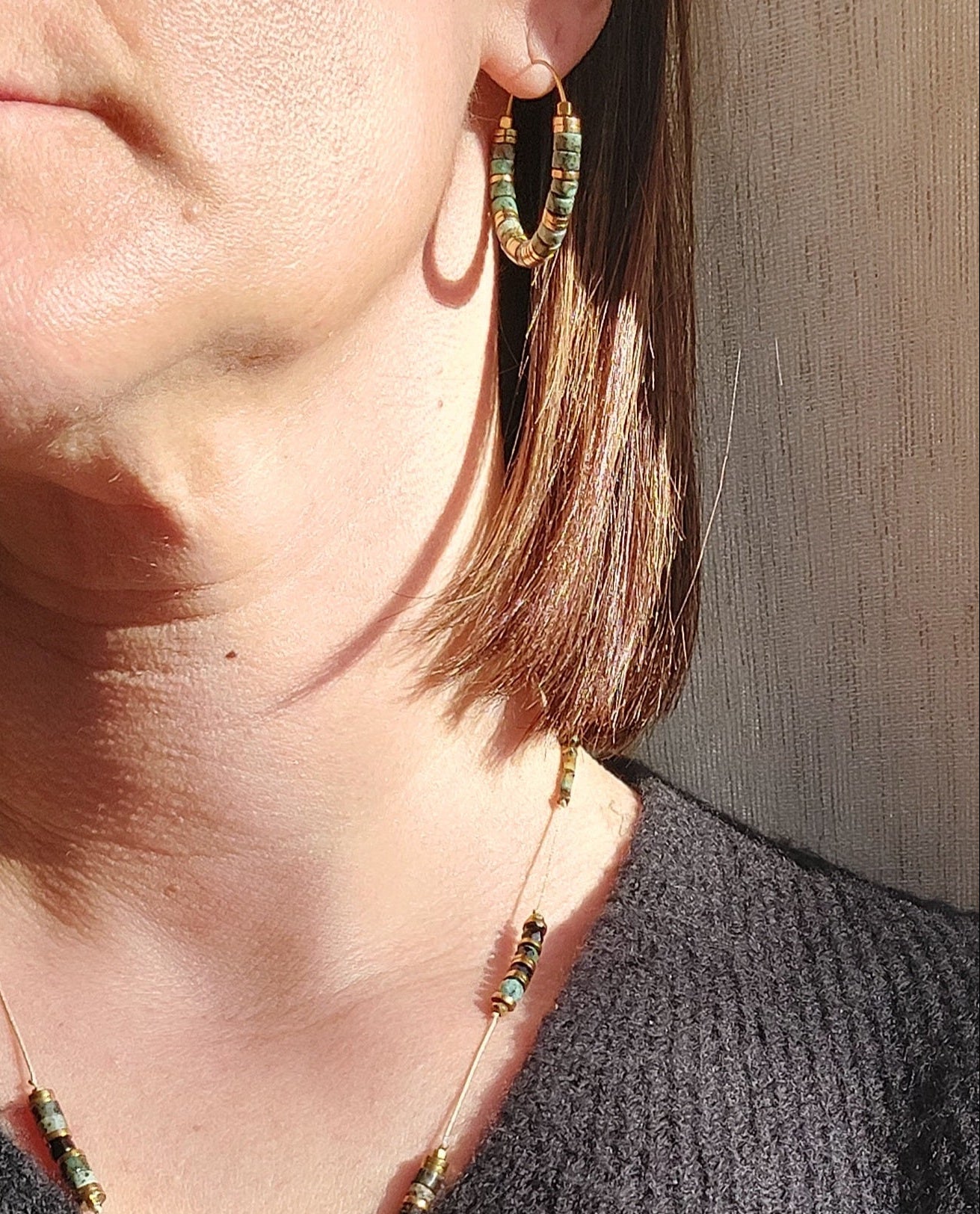 Boucles d’oreilles créoles en perles heishi turquoises africaines portées au soleil, en gros plan, révélant les reflets naturels du bijou bohème fait main.