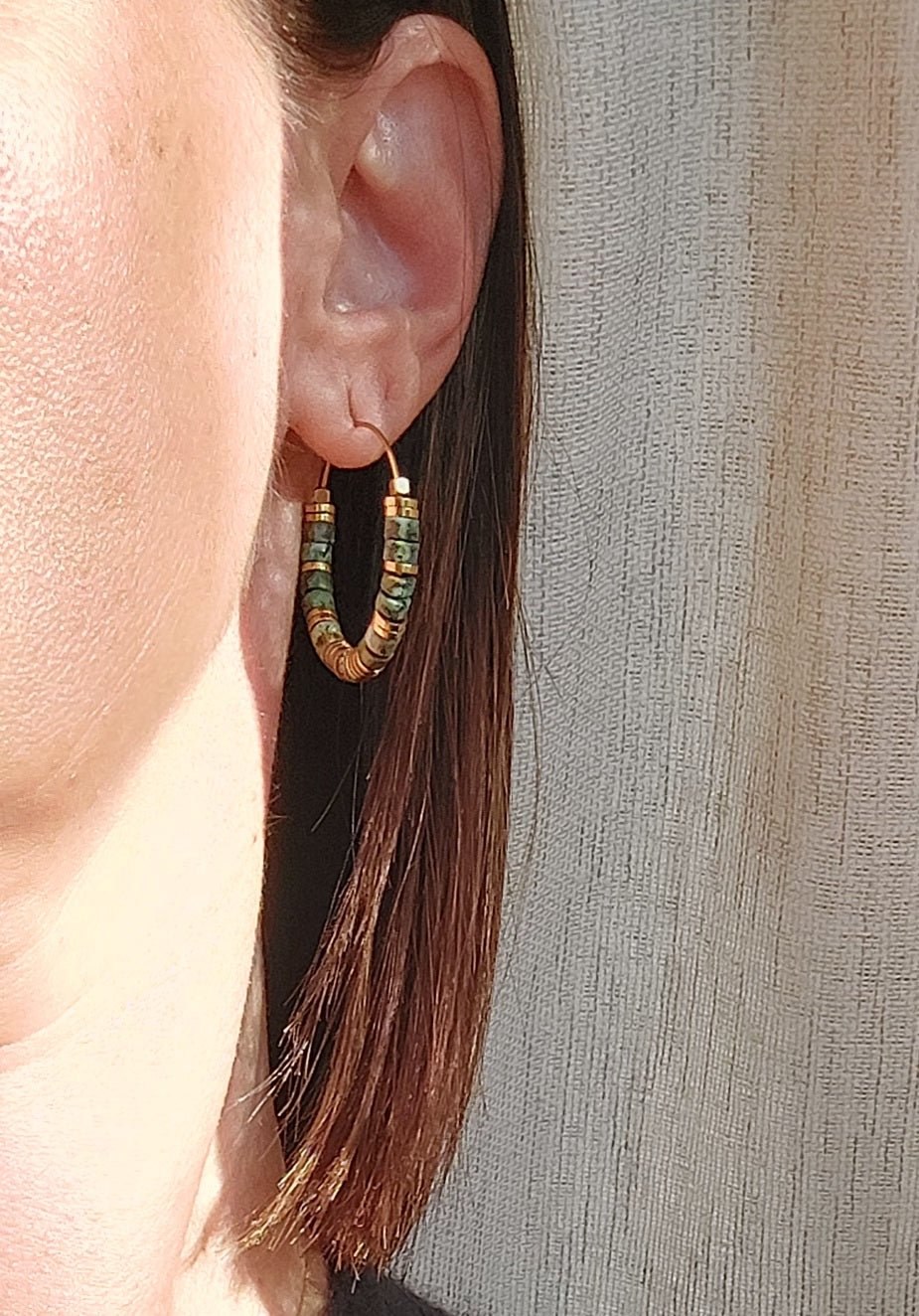 Boucles d’oreilles créoles en perles heishi turquoises africaines portées, avec de subtils reflets naturels de la lumière du soleil sur le bijou bohème fait main.