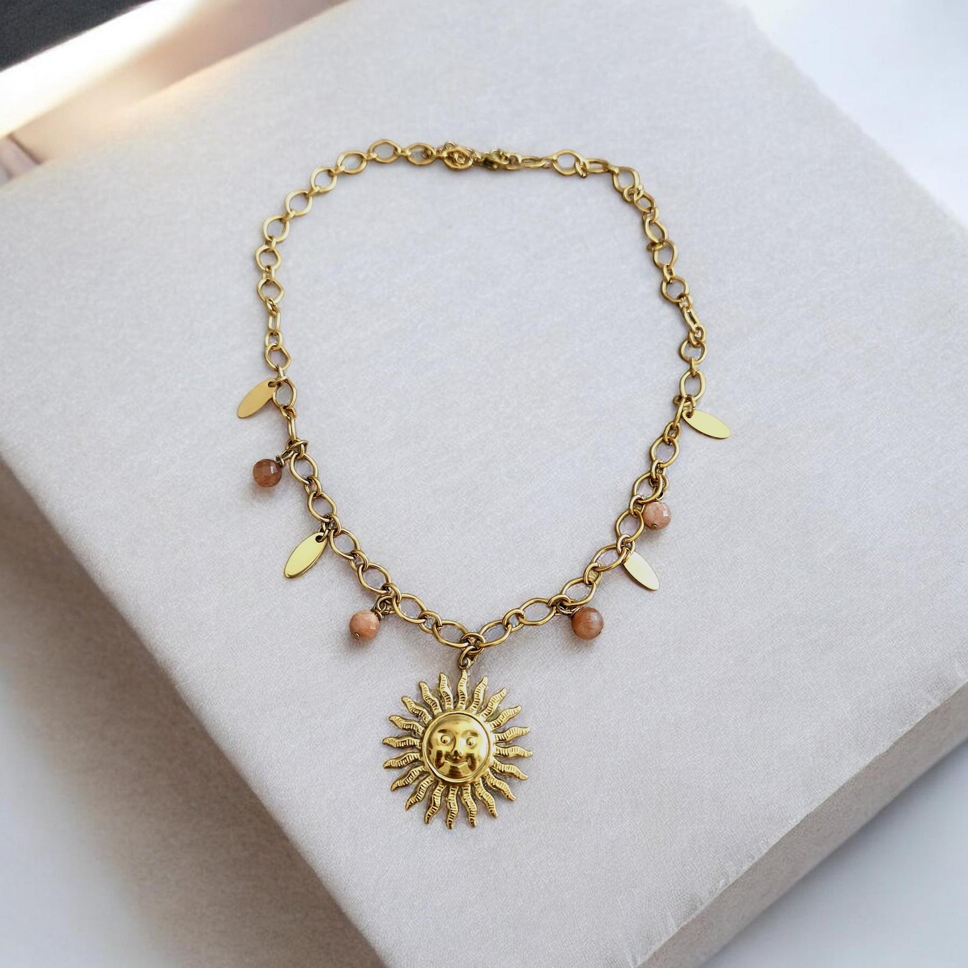 Collier bohème artisanal en acier inoxydable avec pendentif soleil et pampilles ornées de pierres de soleil naturelles, exposé sur présentoir sur fond clair