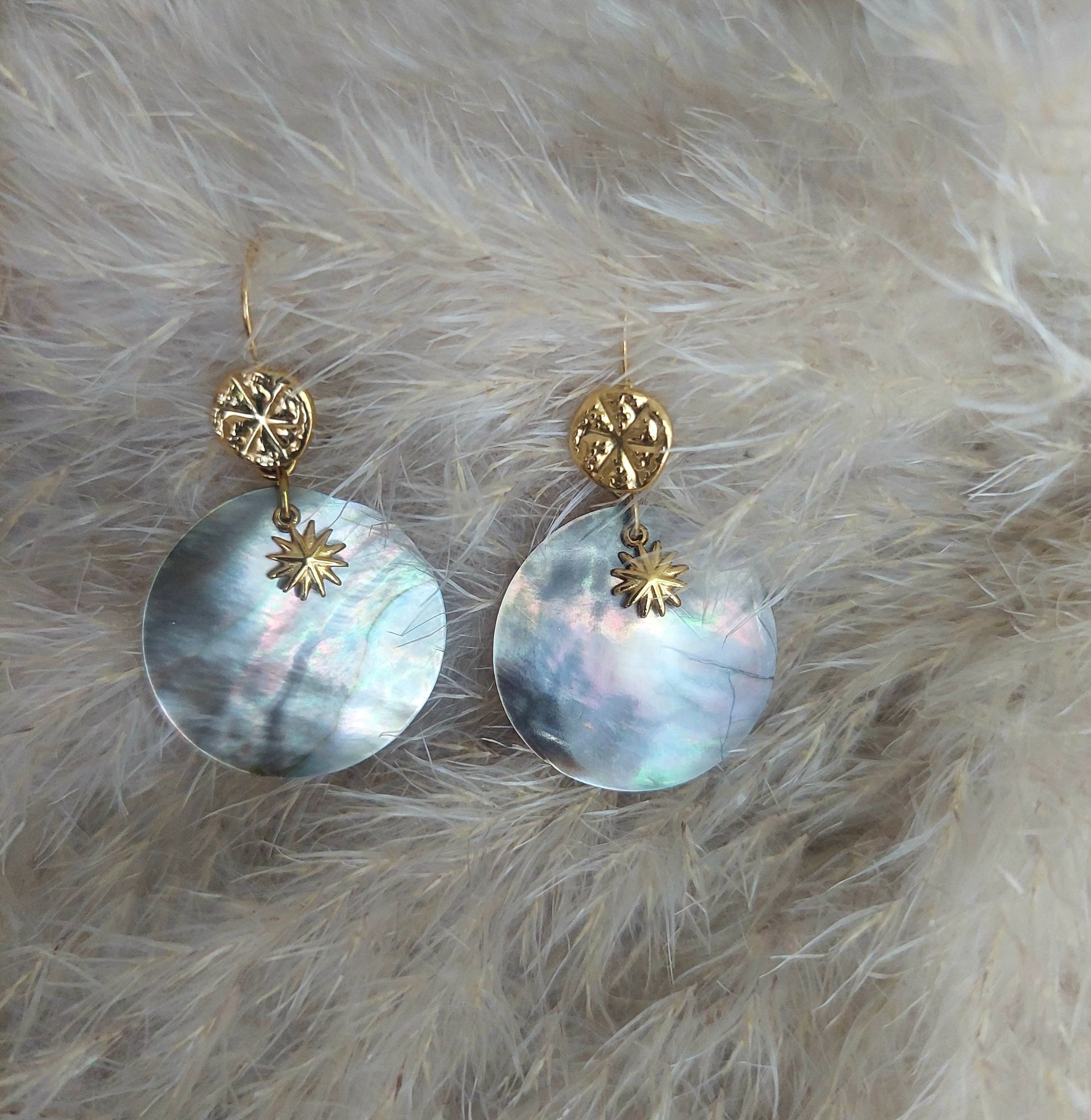 Détail des boucles d’oreilles dormeuses en acier inoxydable, nacre naturelle et mini soleil sur fond clair, style bohème
