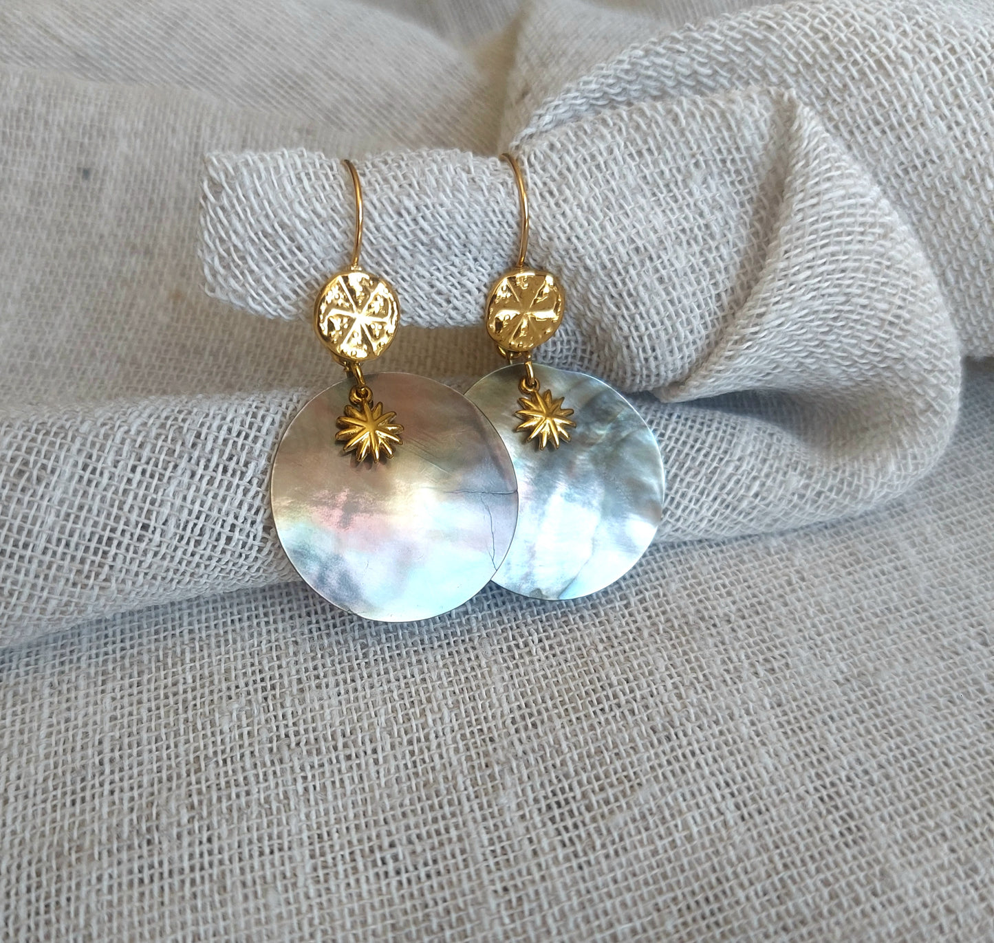 Dormeuses en acier inoxydable avec pendentif nacre naturelle et soleil posées sur fond clair, boucles d'oreilles bohèmes